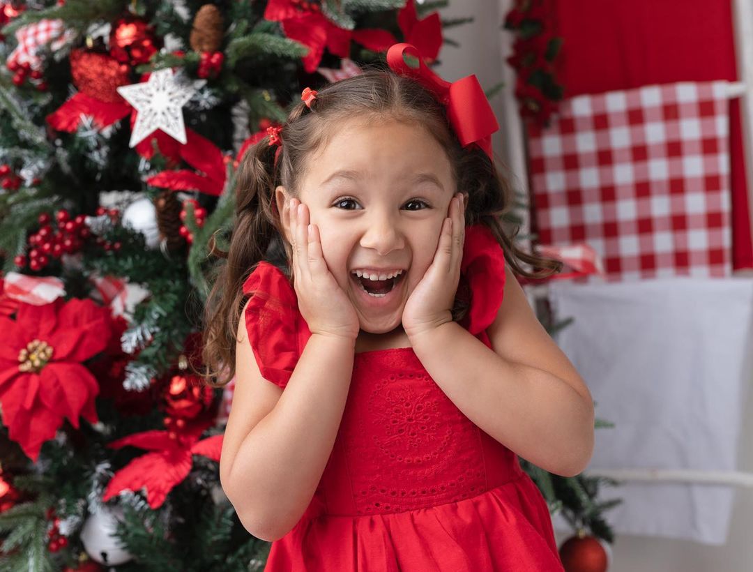 Niña emocionada junto al árbol de Navidad en una sesión de fotos